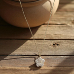 collier fleur blanche et nacree long dore et romantique fiora pose sur fond bois et a cote d un pot en terre cuite