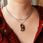 collier long en acier inoxydable au style epure enroule autour et pres du cou avec pendant ovale et brillant ariane