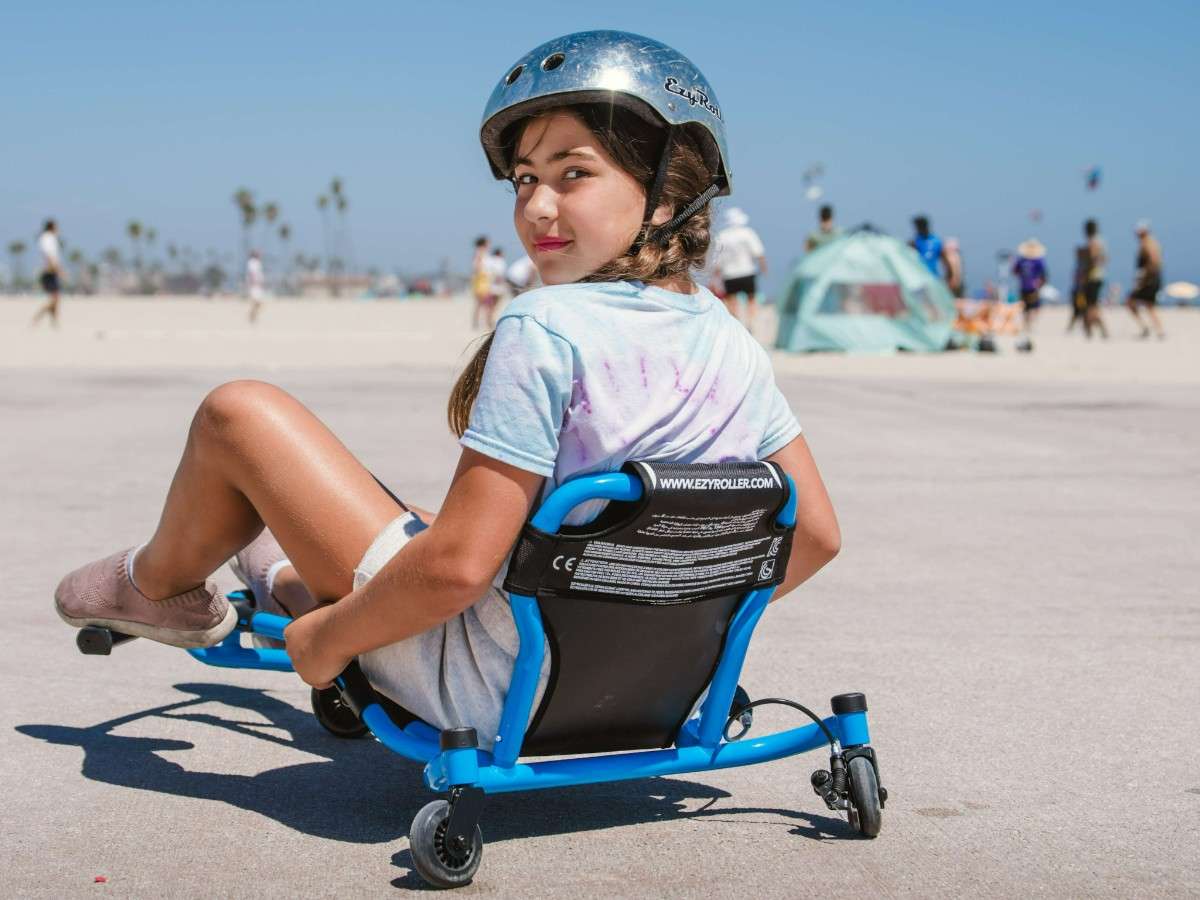Une enfant casquée roule en Ezyroller Spinner X bleu sur une zone dégagée et se retourne vers l’appareil photo.