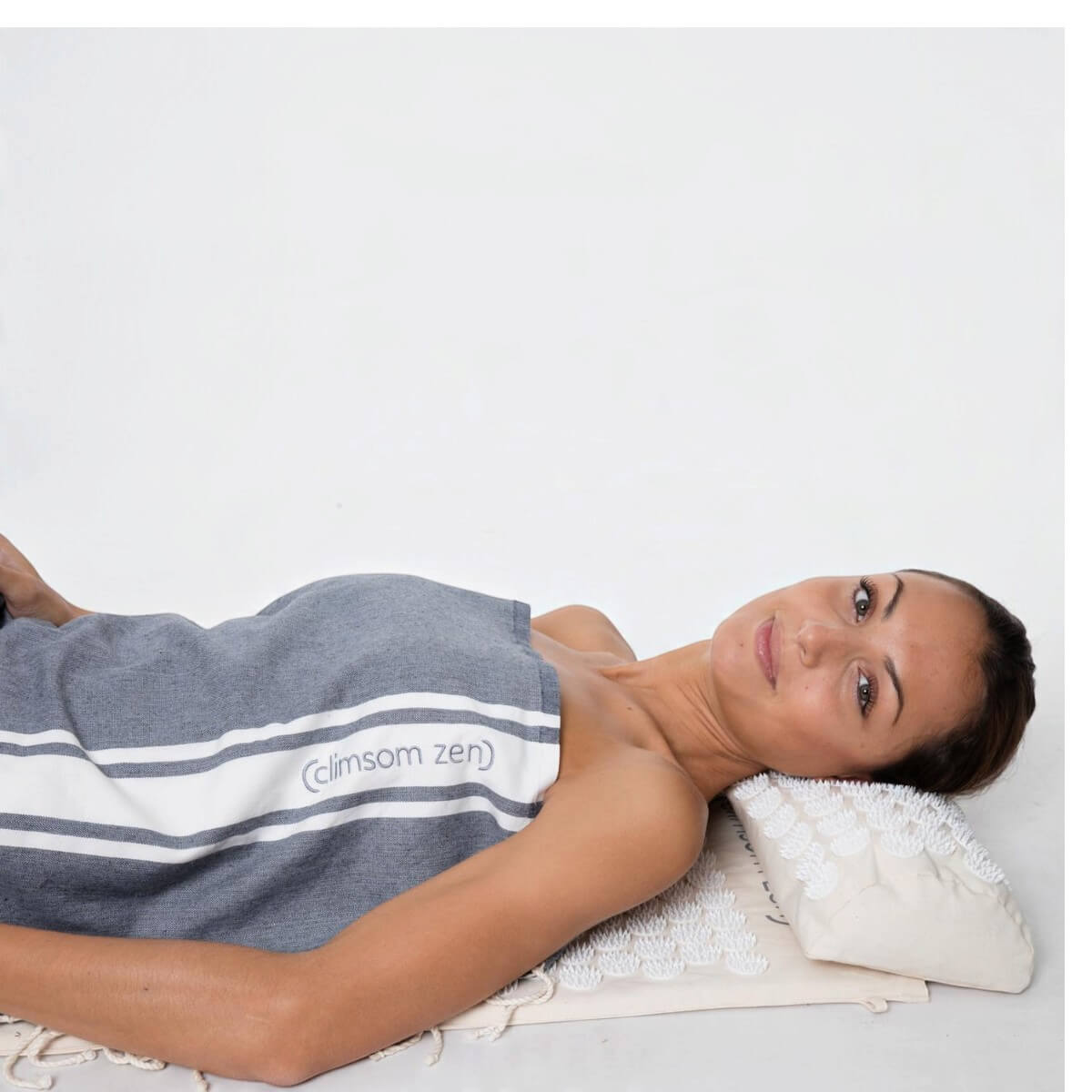Femme allongée sur le tapis d’acupression Climsom Zen à picots blancs, la nuque sur le coussin