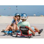 Deux enfants casqués jouent ensemble sur des Ezyroller Spinner X, l’un en rouge et l’autre en bleu, sur une zone dégagée en bord de plage.