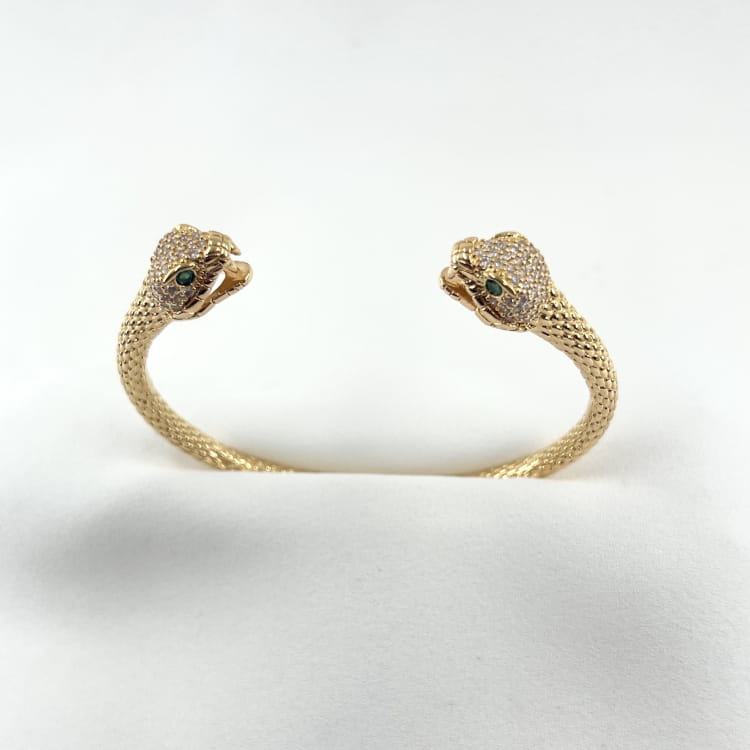 Jonc Dan: Jonc ouvert et écaillé doté de deux têtes de serpent sertis de zirconiums blancs et de zirconiums verts au niveau des yeux. En plaqué or 18 carats