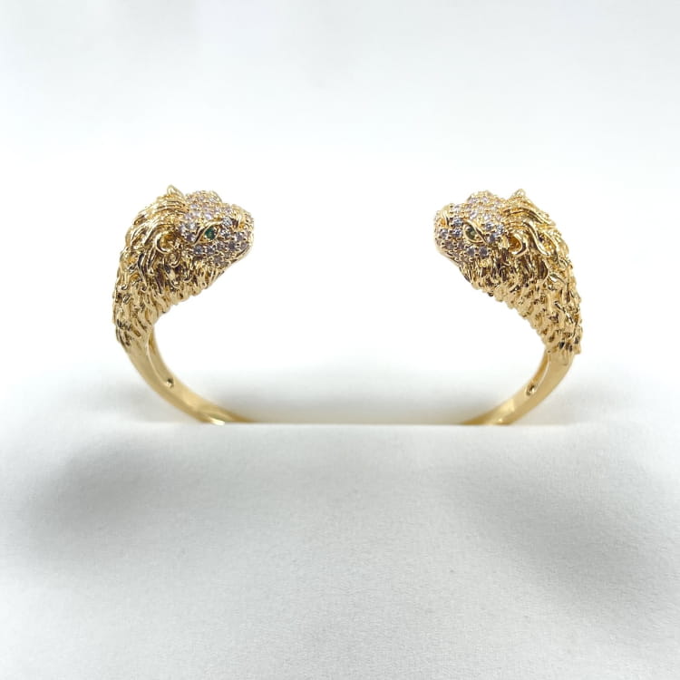 Jonc Leo: Jonc ouvert orné de deux têtes de lion sertis de zironiums blancs et de zirconiums verts au niveau des yeux. En plaqué or 18 carats