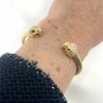 Jonc Dan: Jonc ouvert et écaillé doté de deux têtes de serpent sertis de zirconiums blancs et de zirconiums verts au niveau des yeux. En plaqué or  18 carats