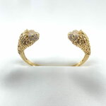 Jonc Leo: Jonc ouvert orné de deux têtes de lion sertis de zironiums blancs et de zirconiums verts au niveau des yeux. En plaqué or 18 carats