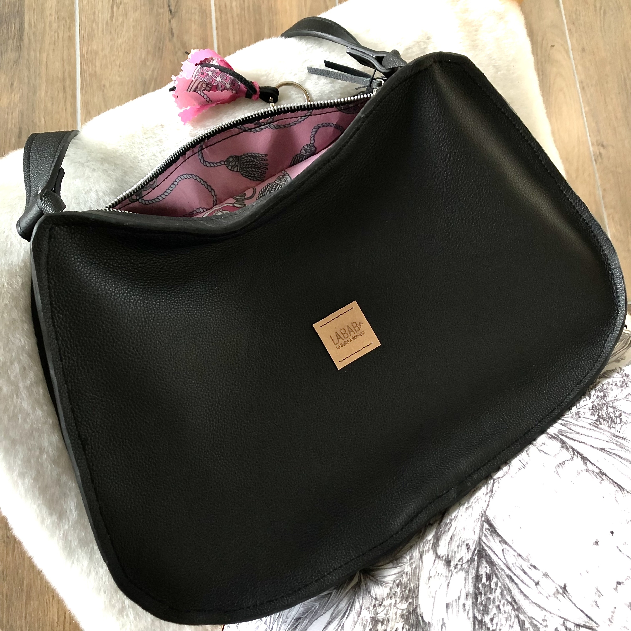 sac cuir noir couché entre ouvert montrant la doublure en foulard souvenir rose et bijoux de sac assorti