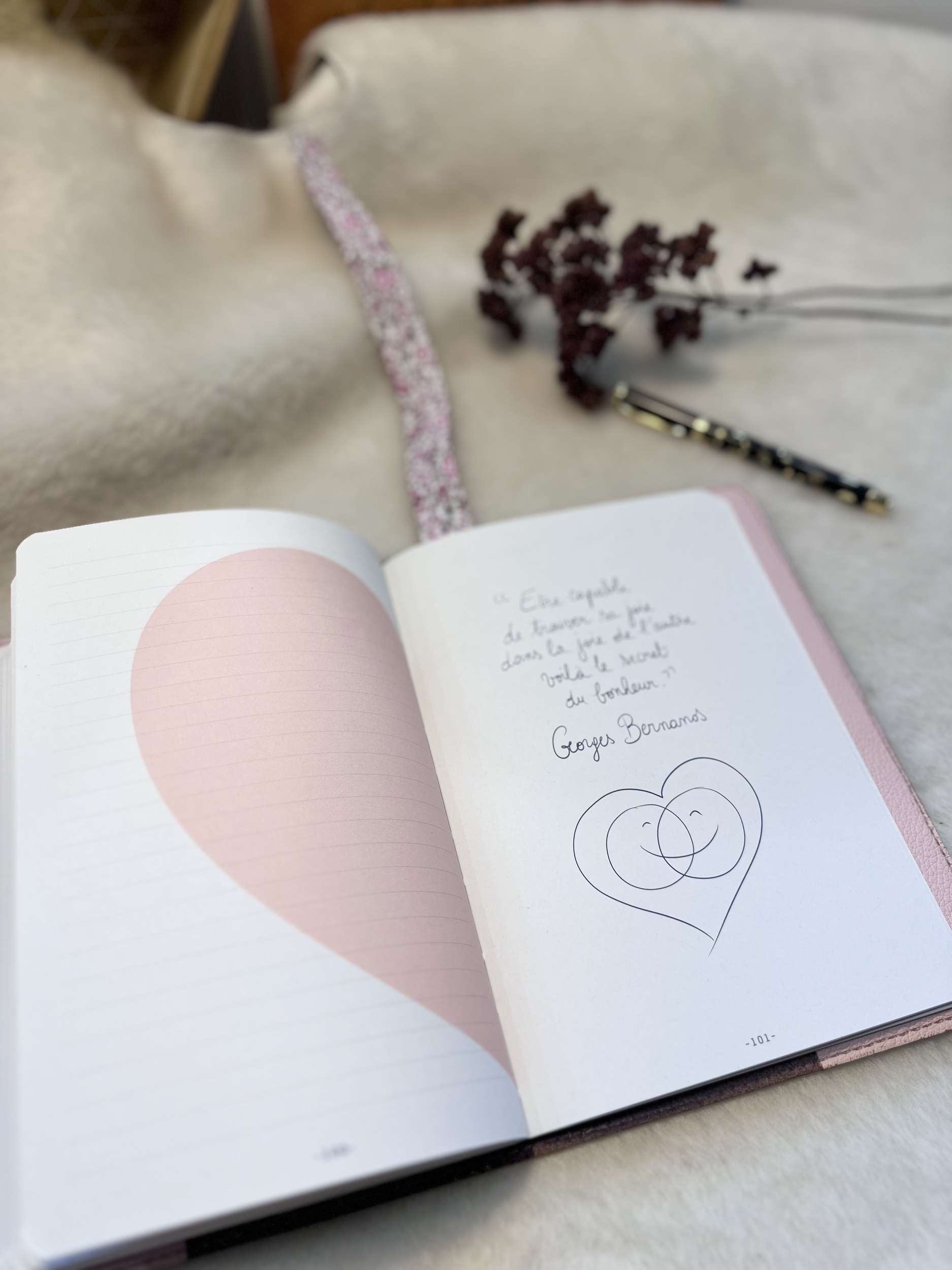 Carnet et protège-carnet ouverts: sur la page de droite une citation sur le bonheur et sur la gauche, un demi cœur rose