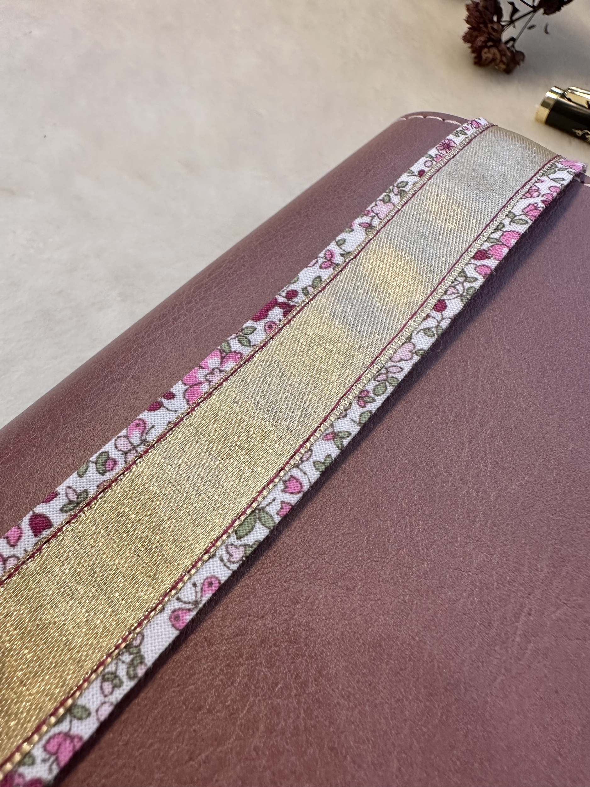 détails du marque-page: tissu fleuri vieux rose et vert sur fond blanc et ruban doré, piqûre contrastante prune sur doré