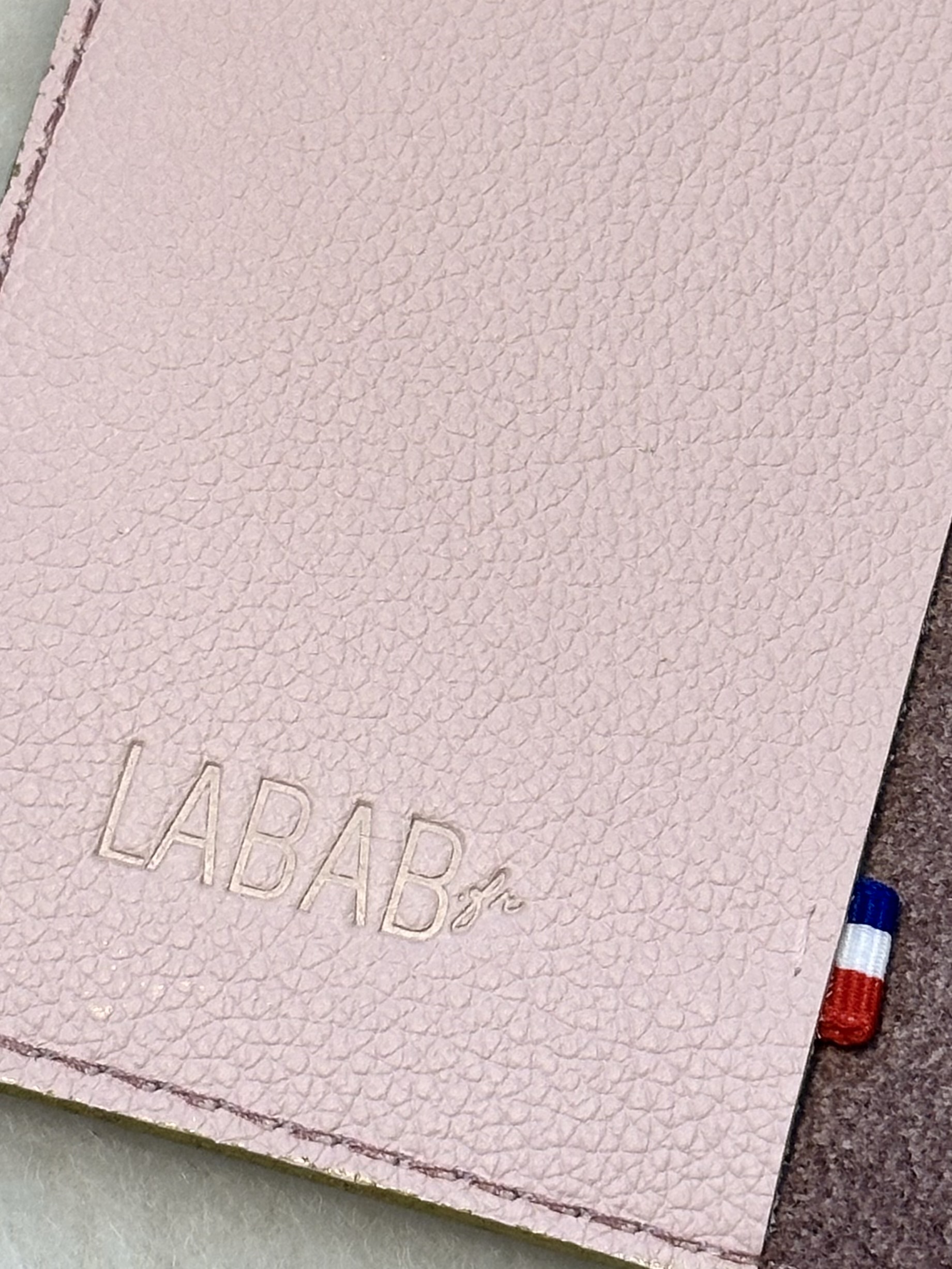 Détails du rabat en cuir grainé rose pâle avec ruban tricolore cousu et marquage à chaud du logo LABAB