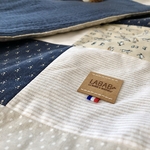 Gros plan détails des tissus des 2 faces ainsi que létiquette logo en cuir végétal ornée dun ruban tricolore