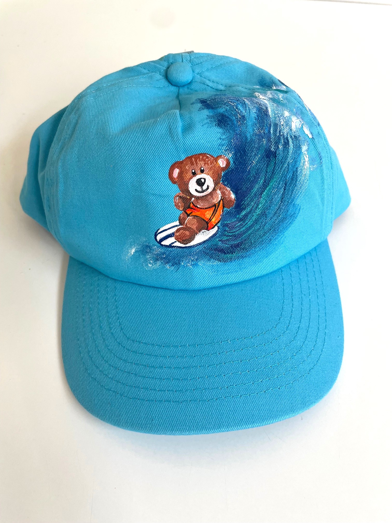 casquette enfant bleue avec un ourson surfeur peint à la main par Elles et No.
