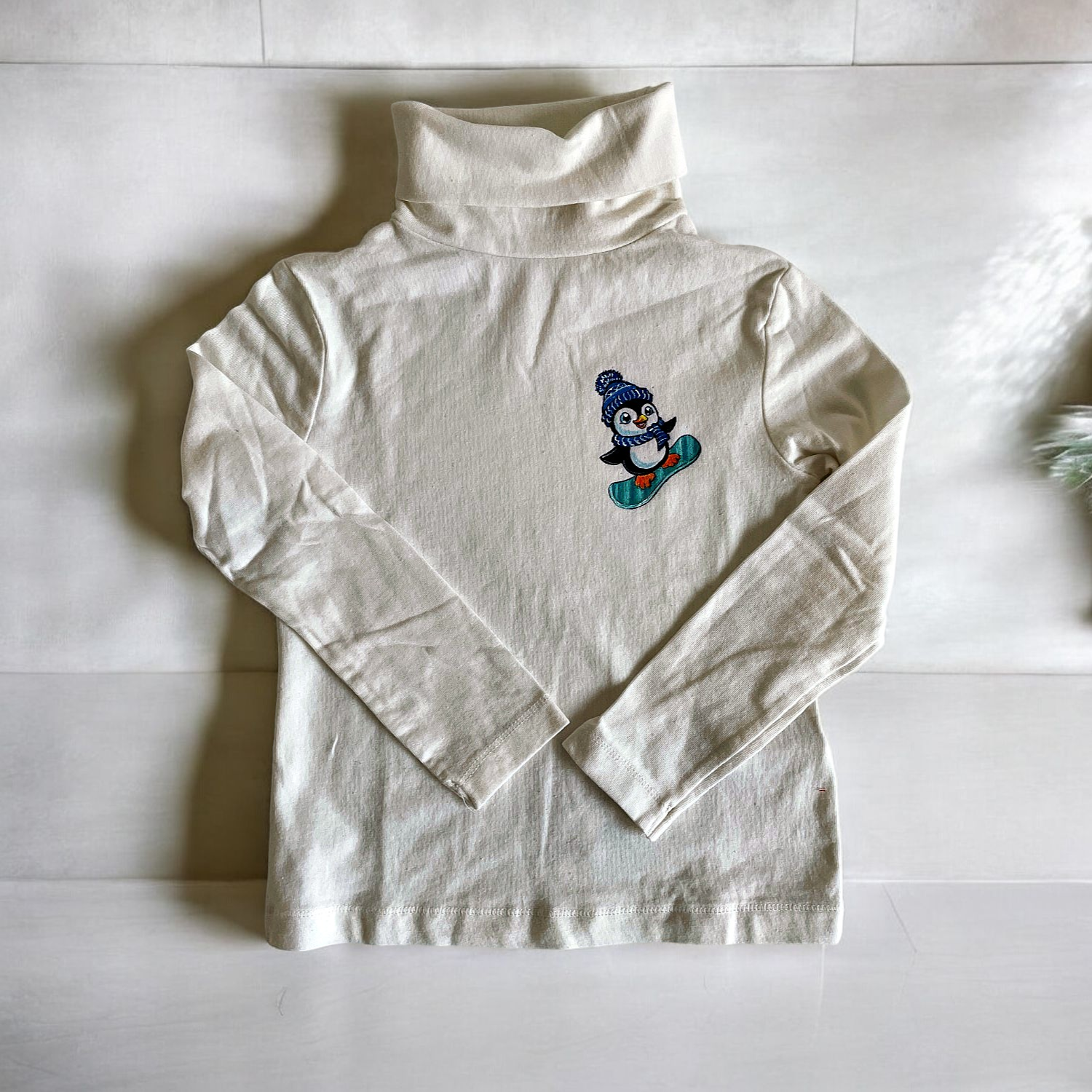 t-shirt col roulé blanc   Elles et No. avec un pingouin rigolo sur son snowboard, peint à la main