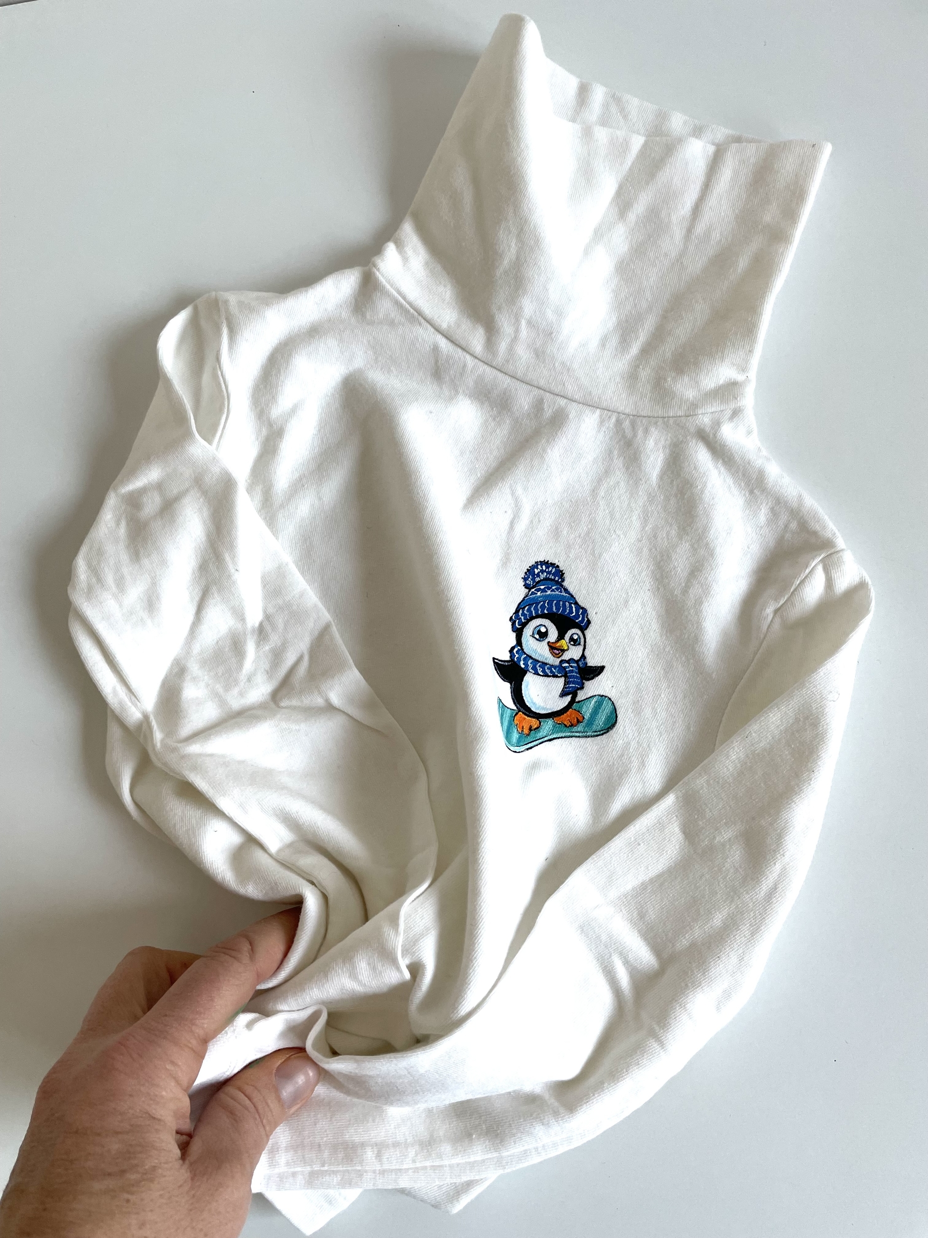 t-shirt col roulé  Elles et No.  avec un pingouin rigolo sur son snowboard, peint à la main
