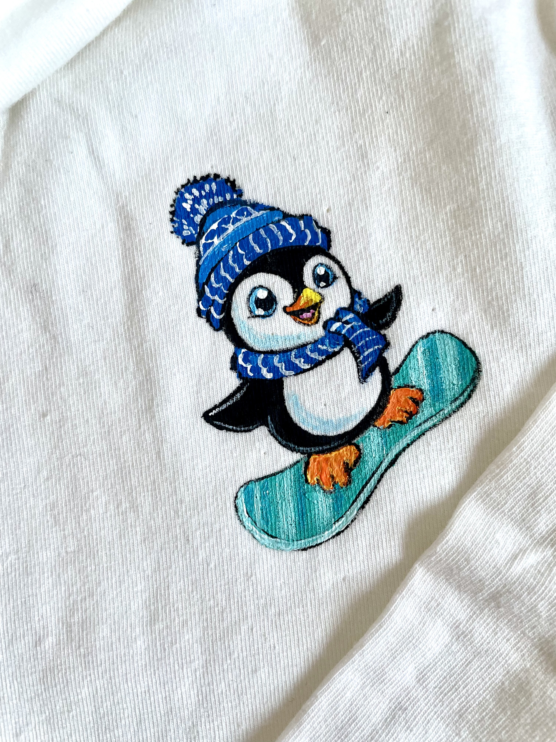 t-shirt col roulé blanc.Elles et No. avec un pingouin rigolo sur son snowboard, peint à la main