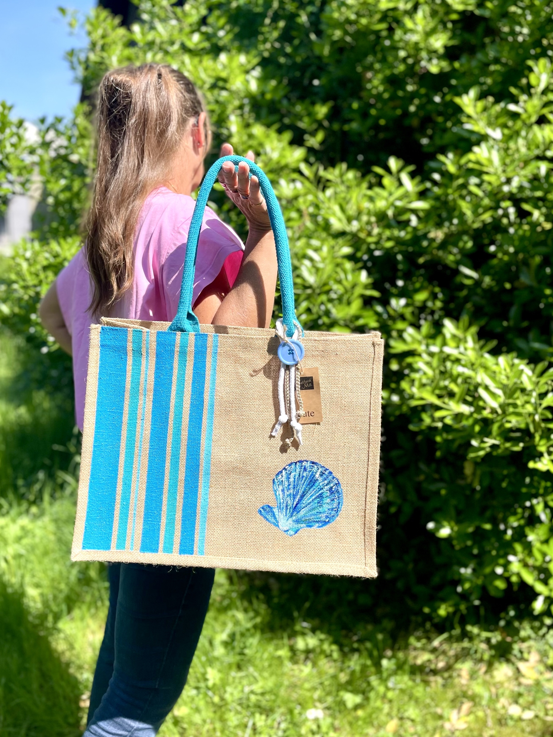 Igrand sac de plage en jute avec des bandes bayadère bleus et un coquillage peints à la main par Elle et No. Un colifichet original est attaché à la anse.