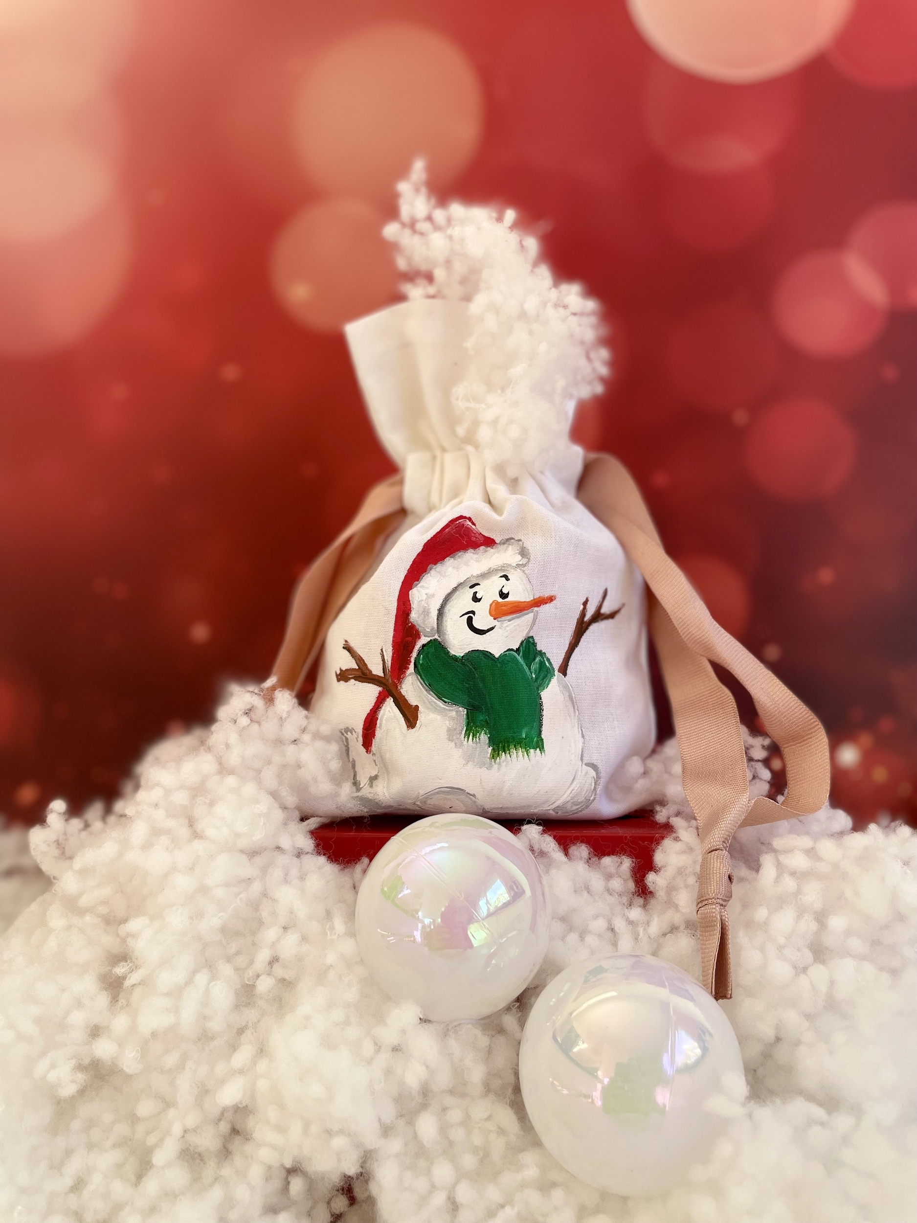 Pochon en coton blanc et ruban de satin rose avec un bonhomme de neige portant un bonnet de Père Noël peint à la main par Elles et No.