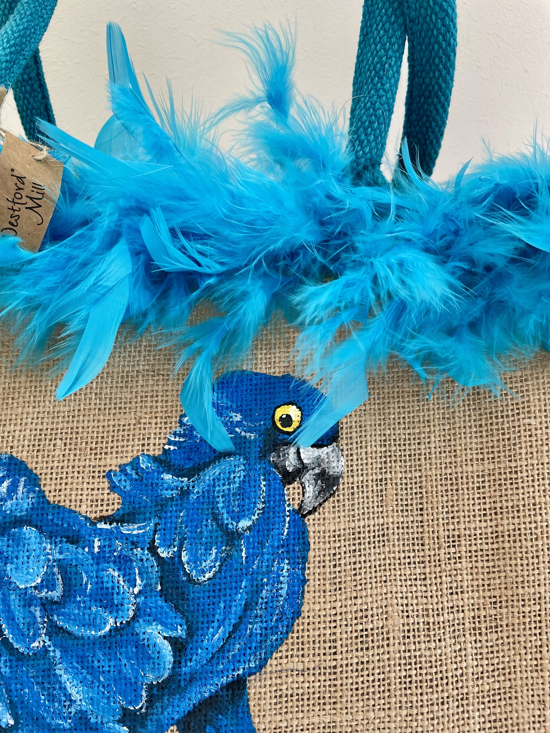 Sac de plage en jute avec des perroquets bleus peints à la main par Elles et No. et un boa en plumes collés sur le bord du sac