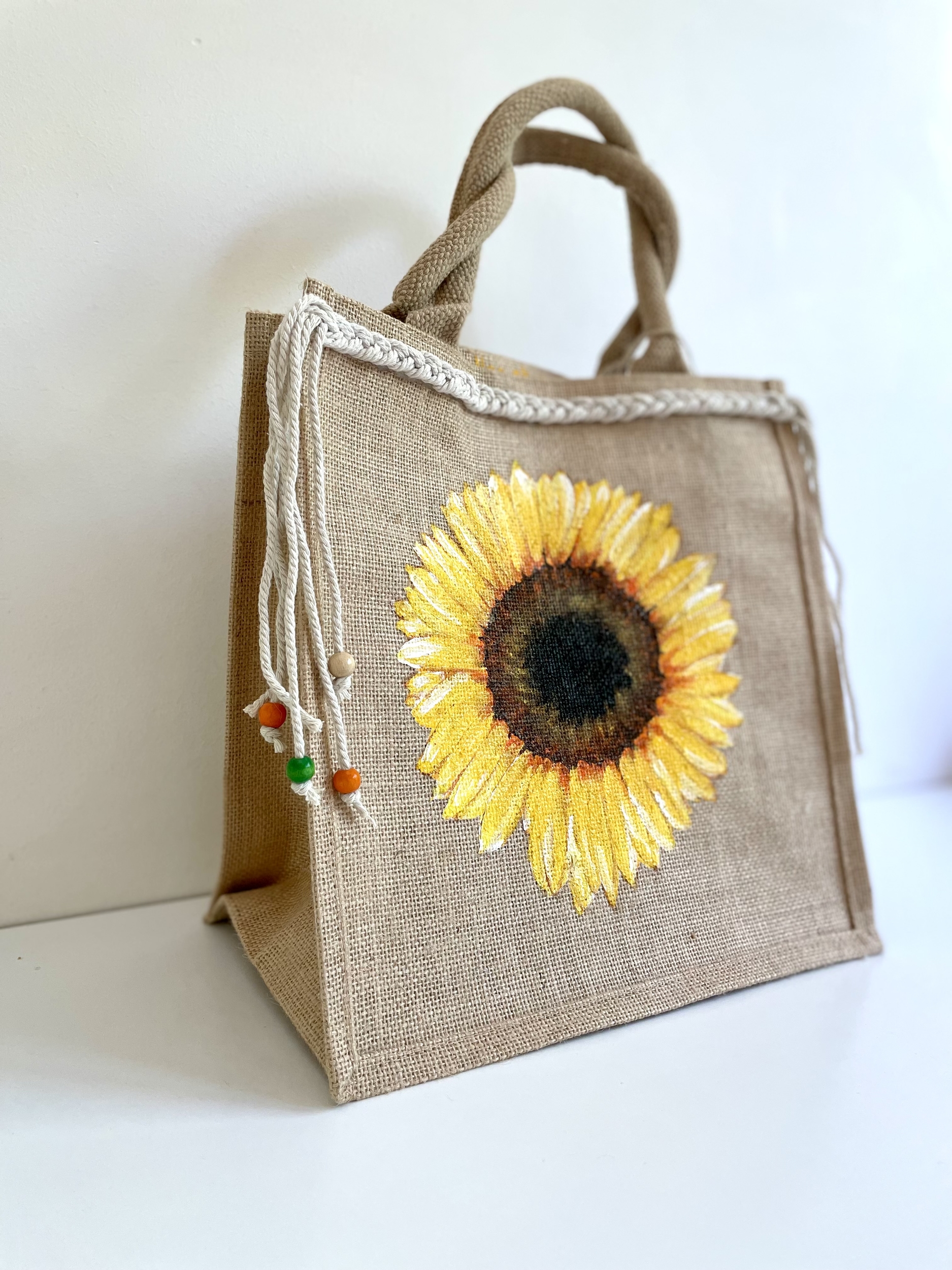 sac en jute avec un tournesol peint à la main par Elles et No. et une tresse en macramé collée sur le bord supérieur du sac.