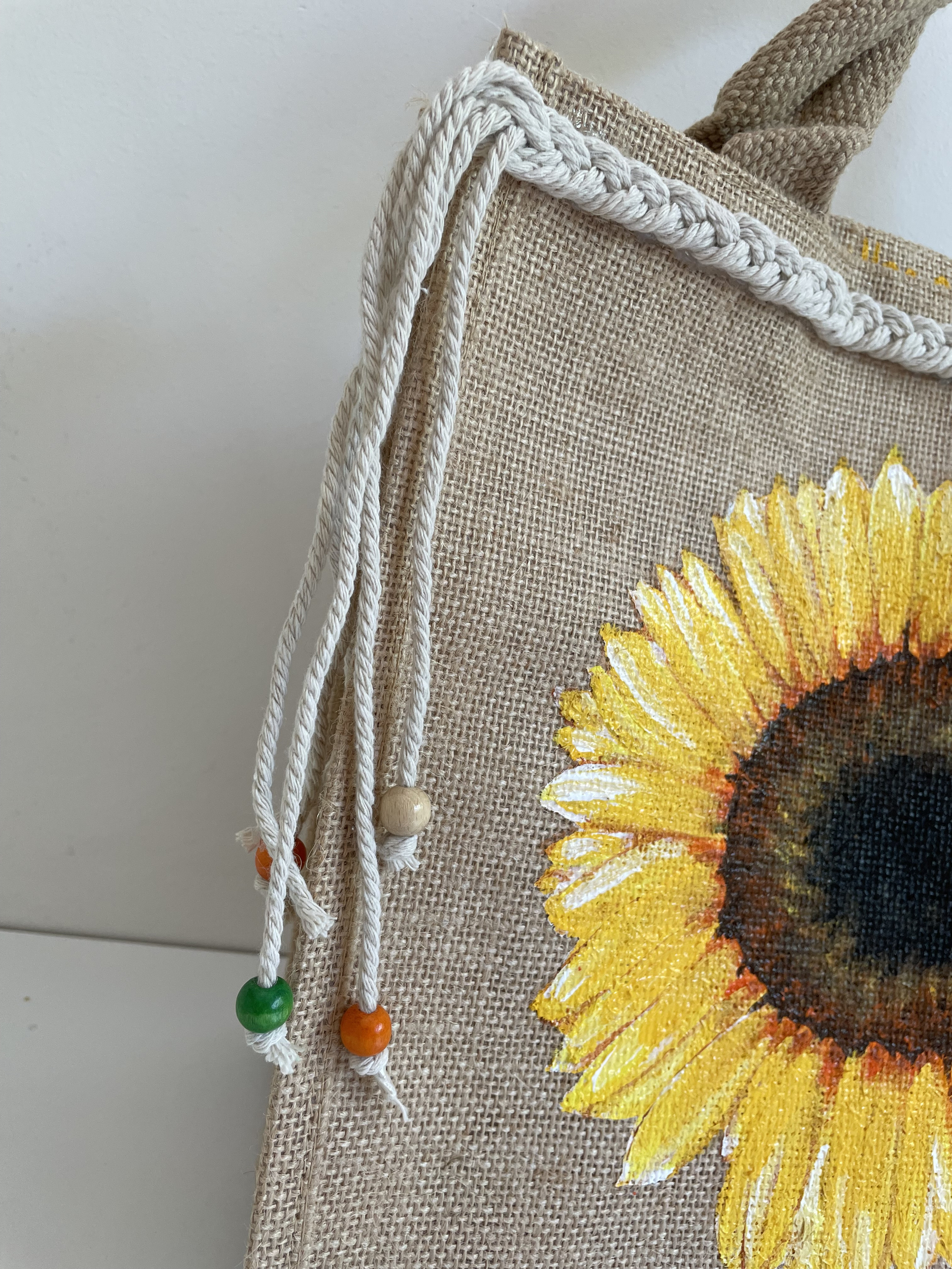sac en jute avec un tournesol peint à la main par Elles et No. et une tresse en macramé collée sur le bord supérieur du sac.