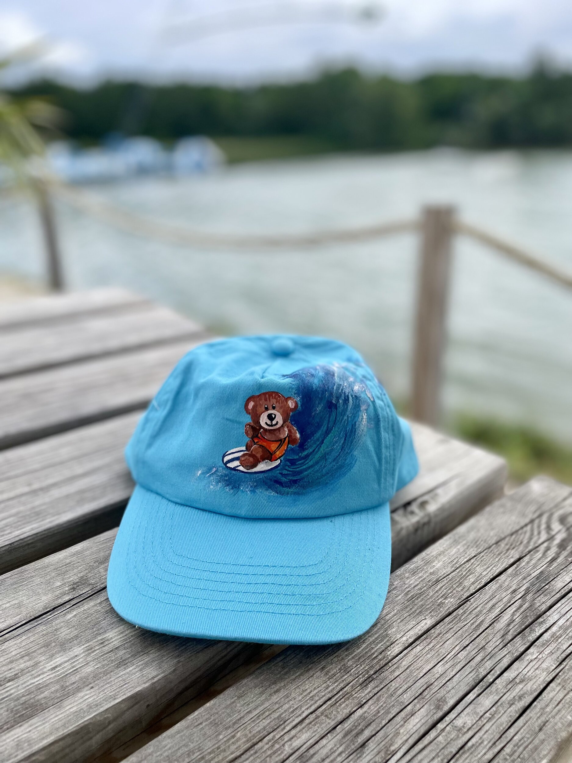 Casquette enfant en coton bleu ciel avec un ourson surfeur peint à la main par Elles et No.