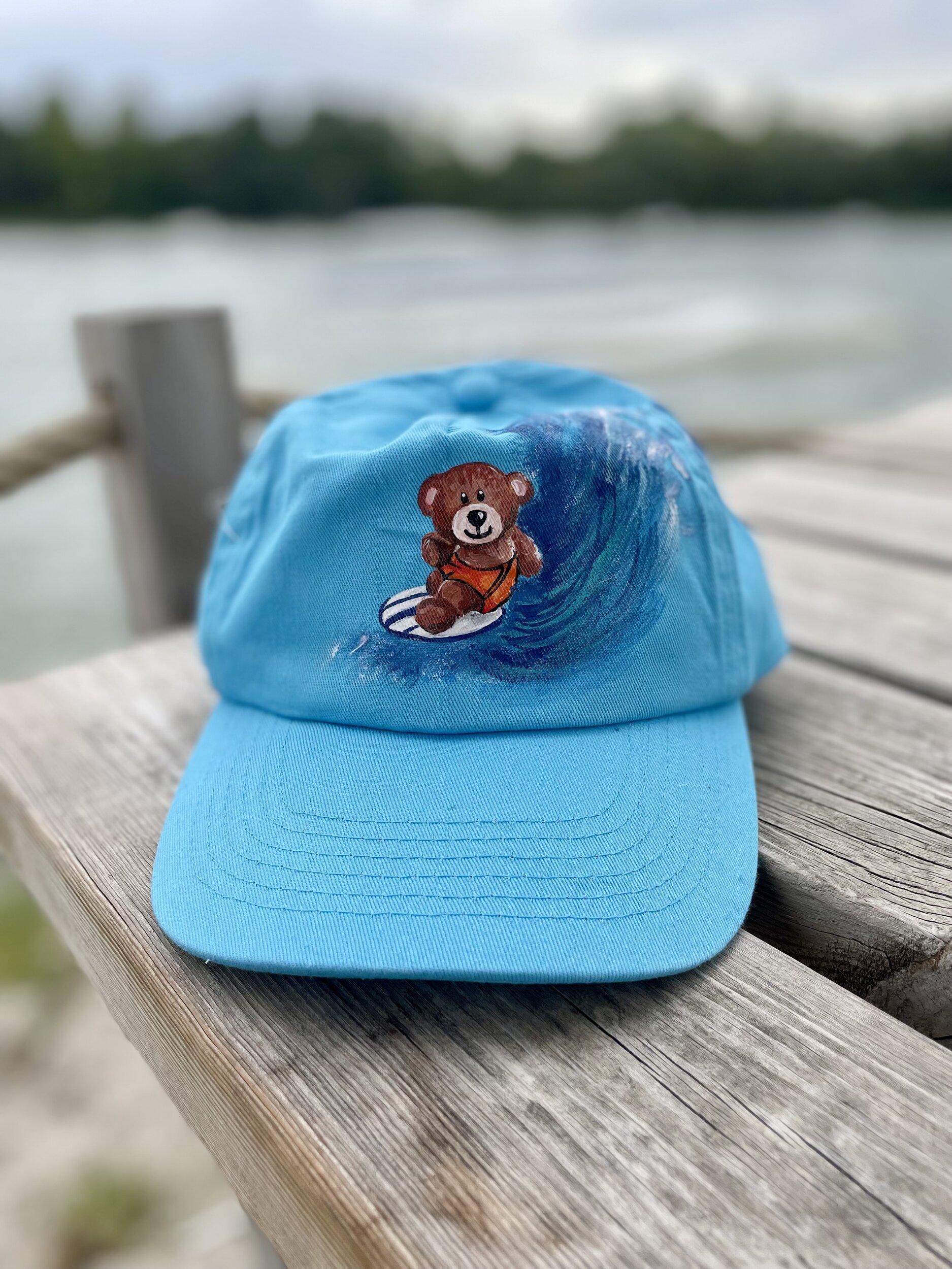 Casquette enfant en coton bleu ciel avec un ourson surfeur peint à la main par Elles et No.