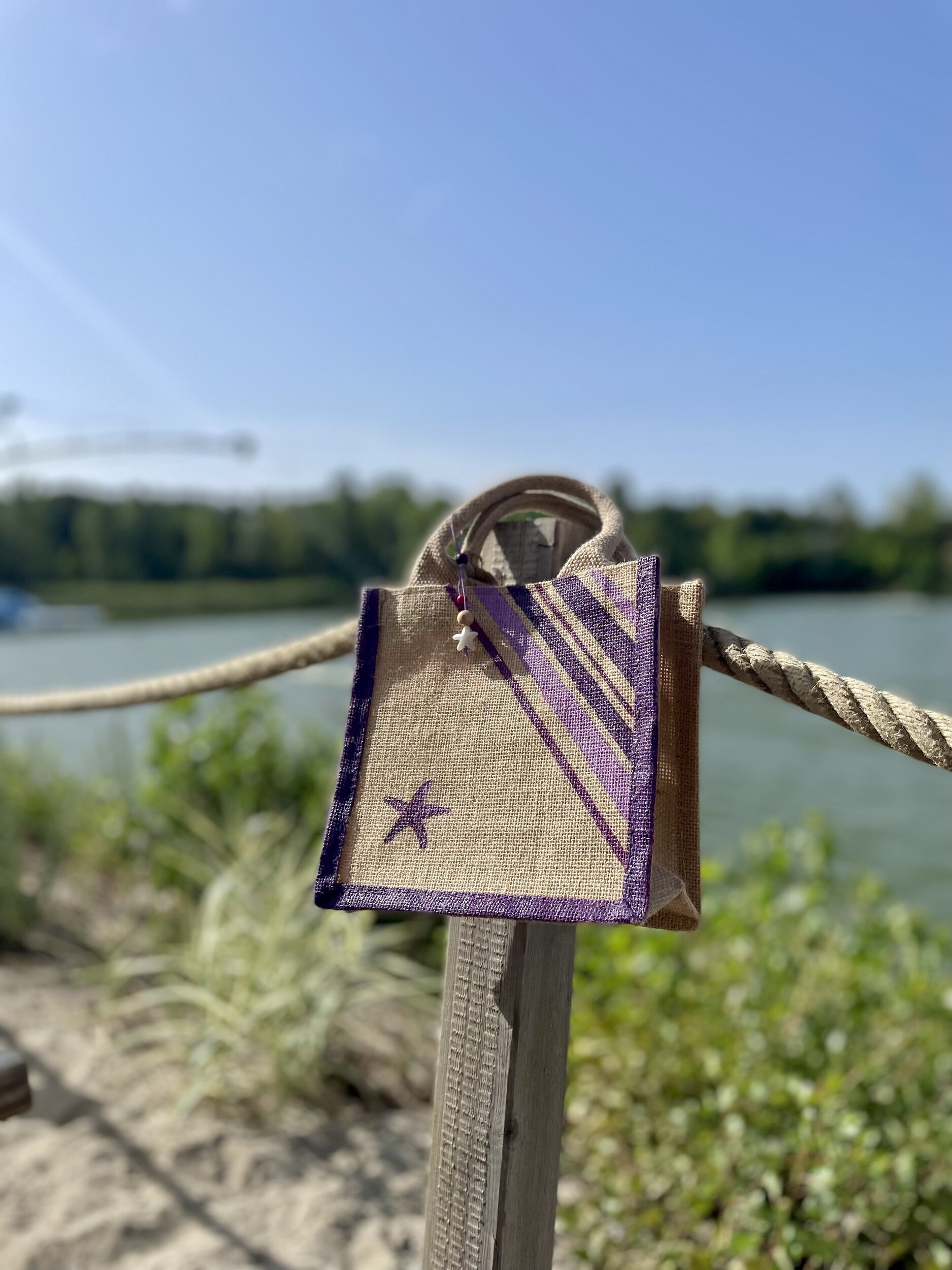 tout petit sac de plage en jute avec des rayures bayadère dans les tons violets et une étoile de mer, peints à la main par Elles et No., présenté au bord de leau