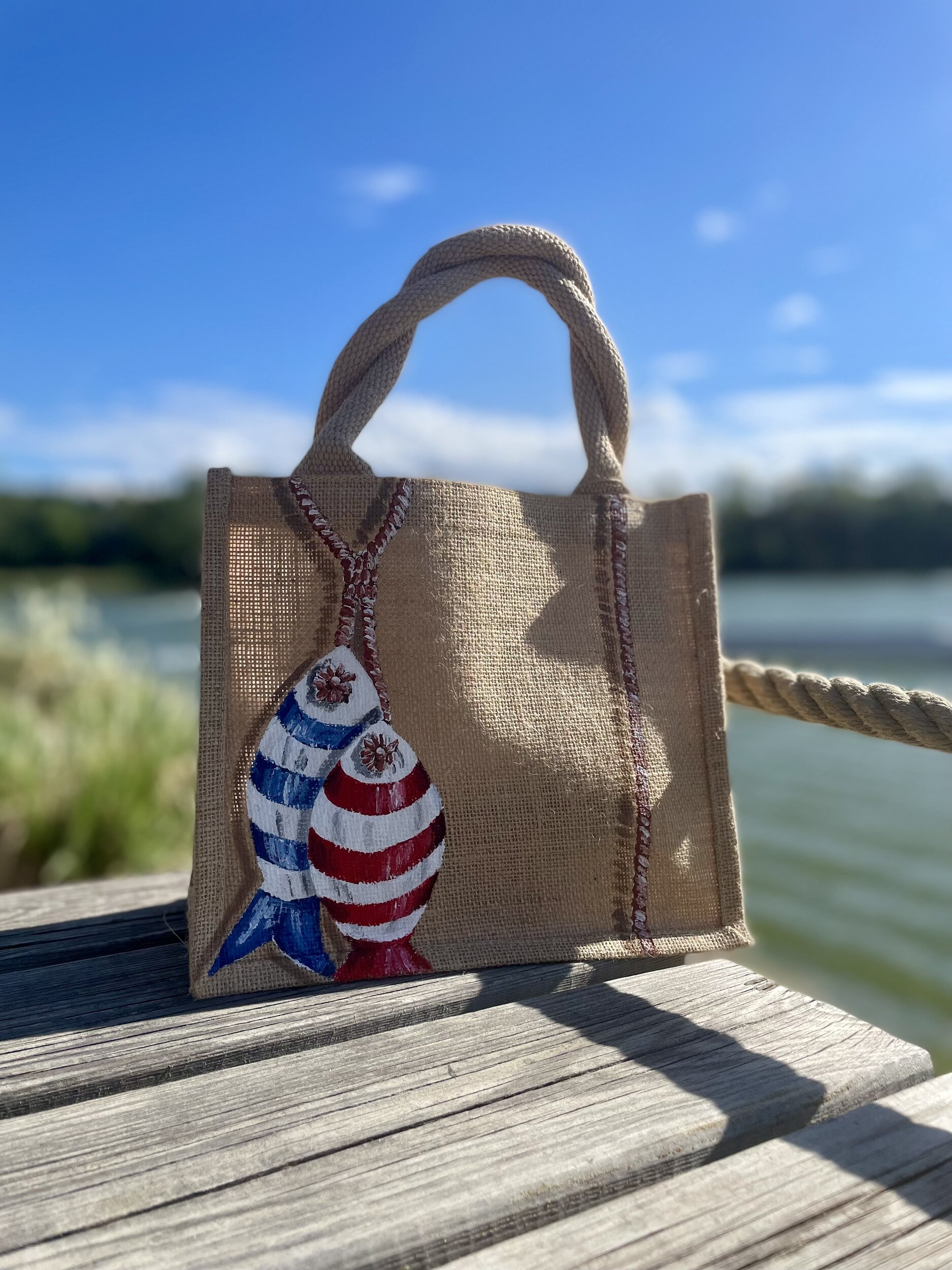 Sac en jute Saint-Malo avec des poissons style poissons en bois peints à la main par Elles et No., présenté à la plage