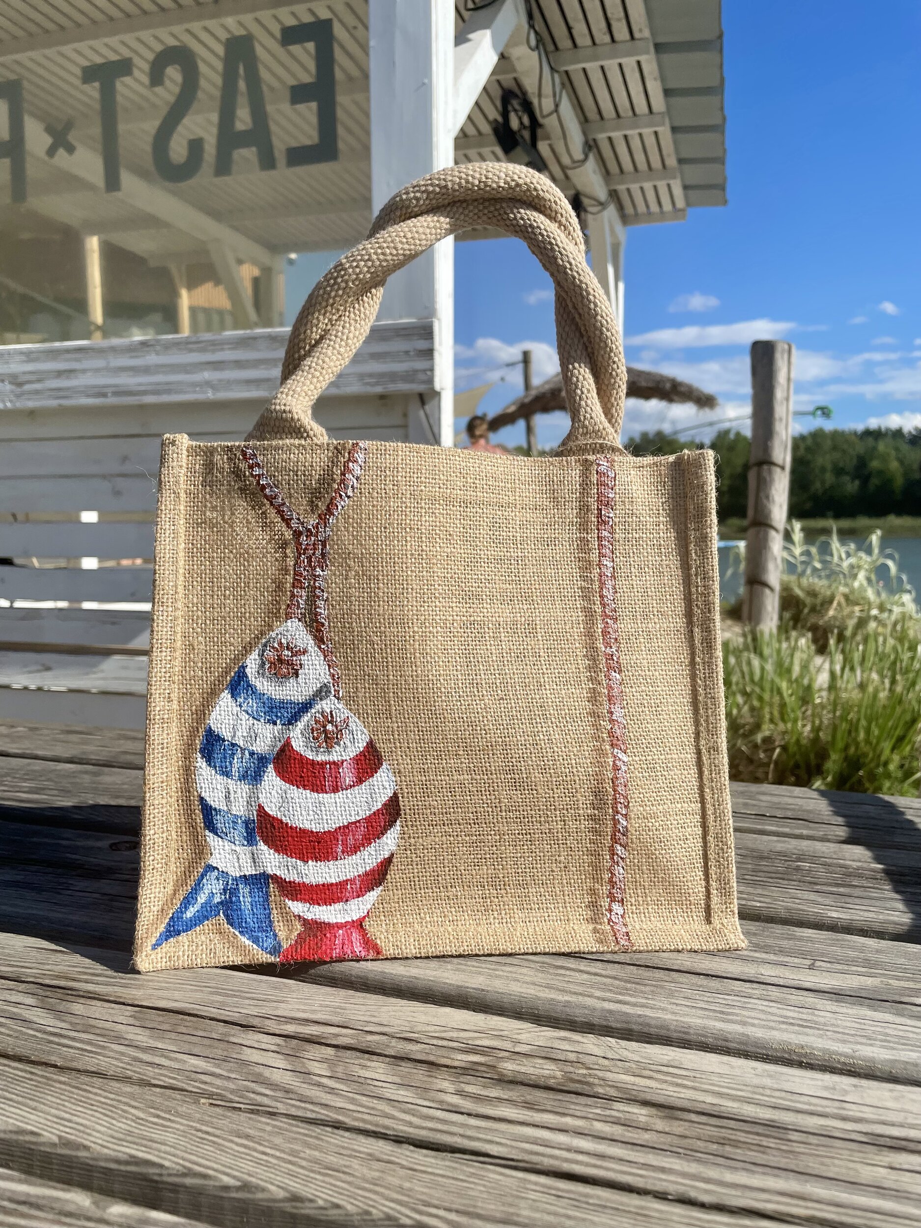 Sac en jute Saint-Malo avec des poissons style poissons en bois peints à la main par Elles et No., présenté à la plage