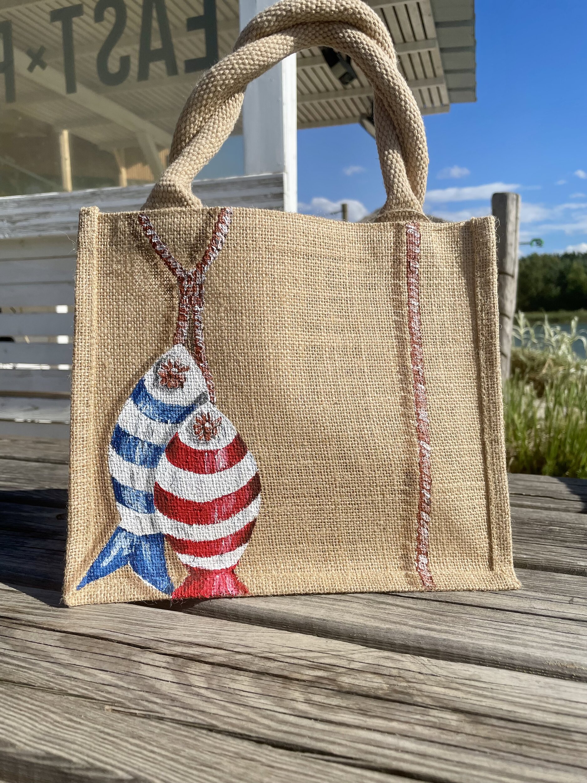 Sac en jute Saint-Malo avec des poissons style poissons en bois peints à la main par Elles et No., présenté à la plage