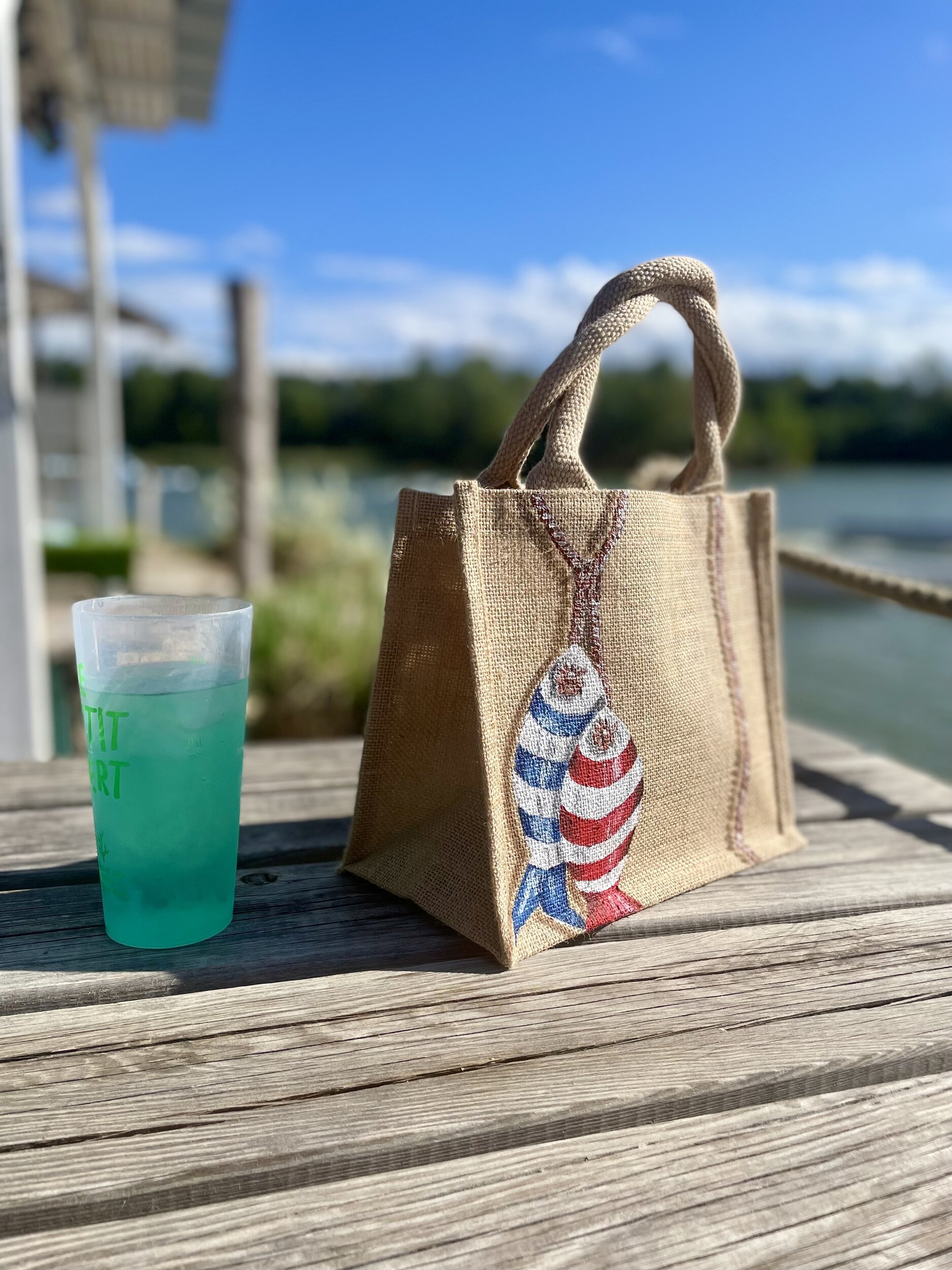 Sac en jute Saint-Malo avec des poissons style poissons en bois peints à la main par Elles et No., présenté à la plage