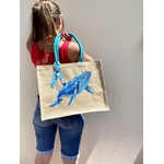 sac de plage en jute avec une baleine bleue peinte à la main par Elles et No., présenté porté par une femme de dos