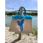 Sac de plage en jute avec des perroquets bleus peints à la main par Elles et No. et un boa en plumes collés sur le bord du sac