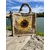 sac en jute avec un gros tournesol peint à la main par Elles et No. et décoré avec une tresse en macramé, présenté au bord de l'eau