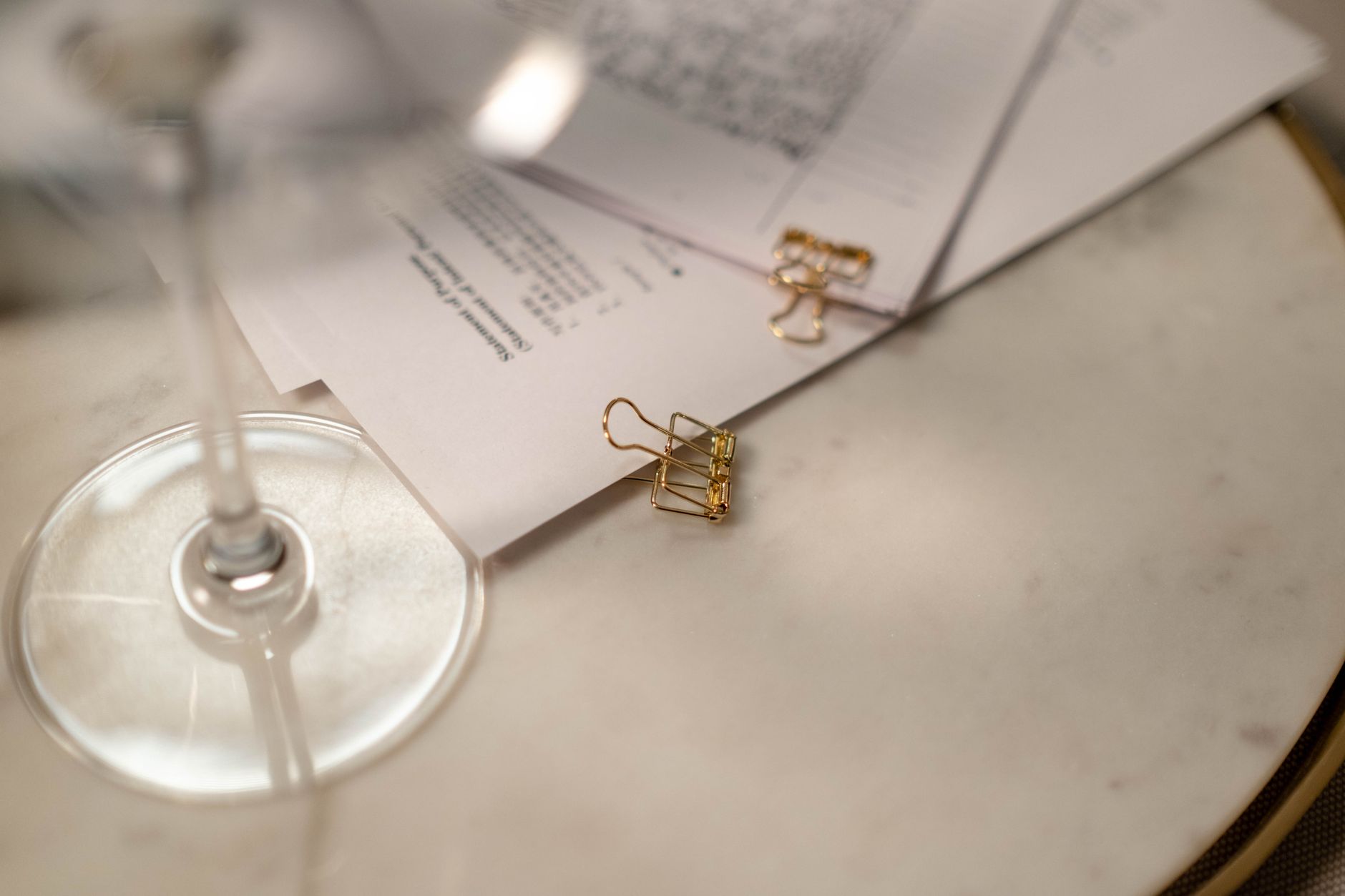 gros plan sur des documents et des trombones sur une table avec un verre de vin montrant un espace de travail raffine