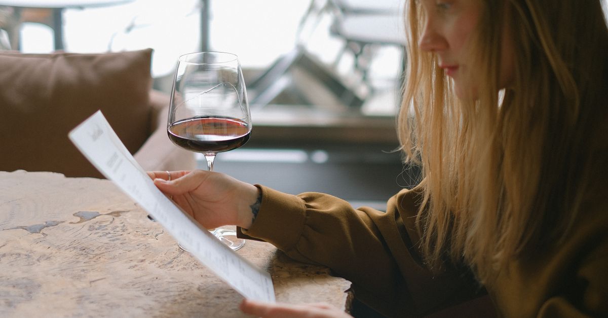 une femme lit un menu tout en tenant un verre de vin rouge dans un restaurant