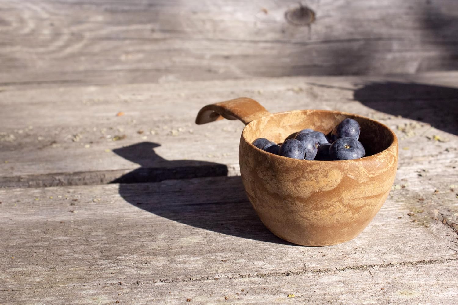 Kuksa Kupilka remplie de myrtilles sur une table en bois patiné