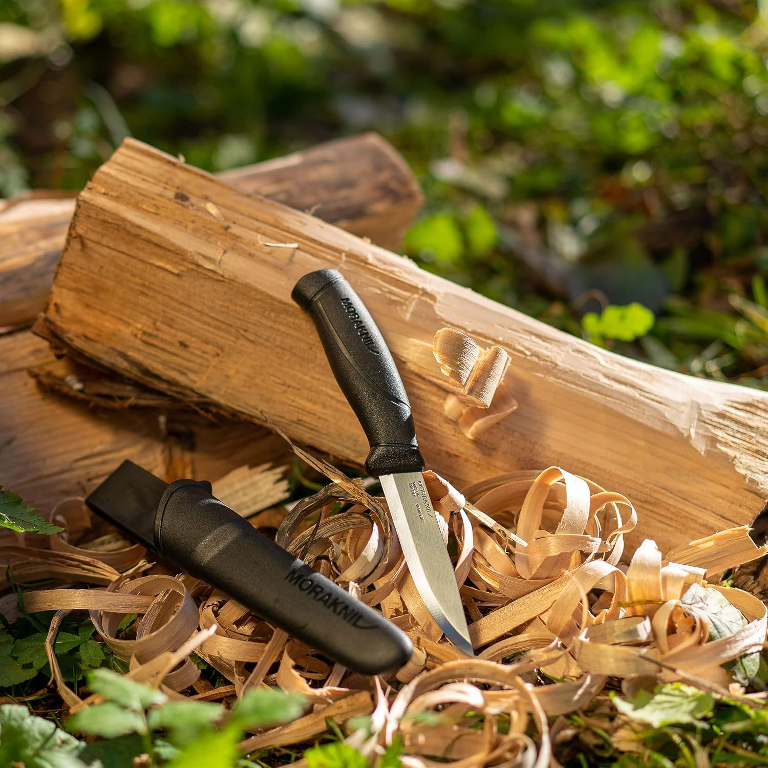 Morakniv Companion noir dressé dans des copeaux contre une bûche fendue, son étui posé à côté