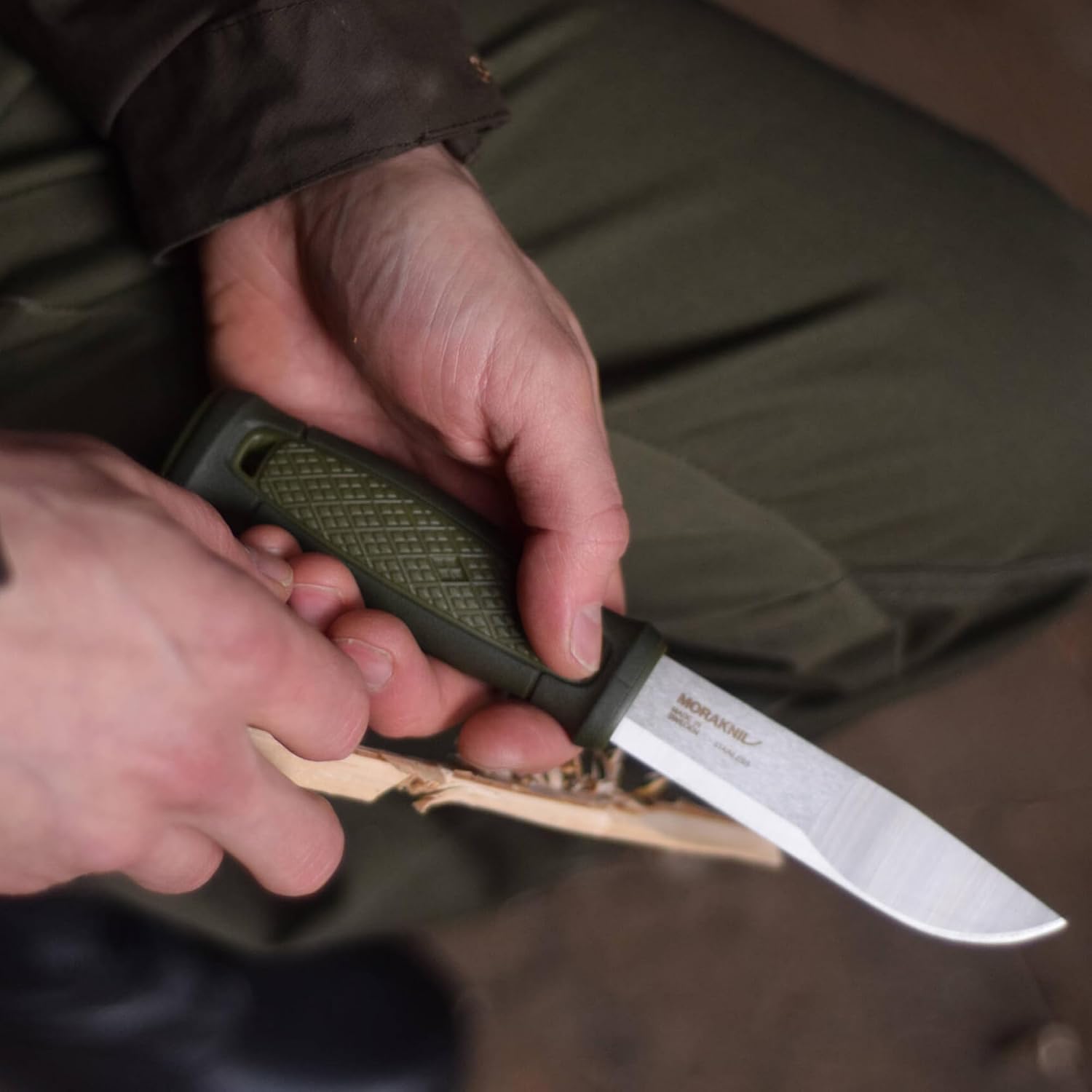 Morakniv Kansbol en main, levant des copeaux fins sur un bâton de bois clair