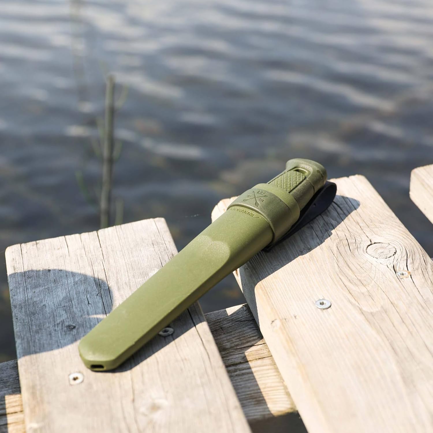 Morakniv Kansbol dans son étui vert, posé sur un ponton en bois au bord dun lac