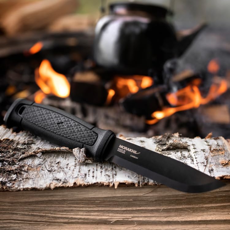 Morakniv Garberg posé sur une bûche de bouleau devant un feu de camp et une bouilloire noire