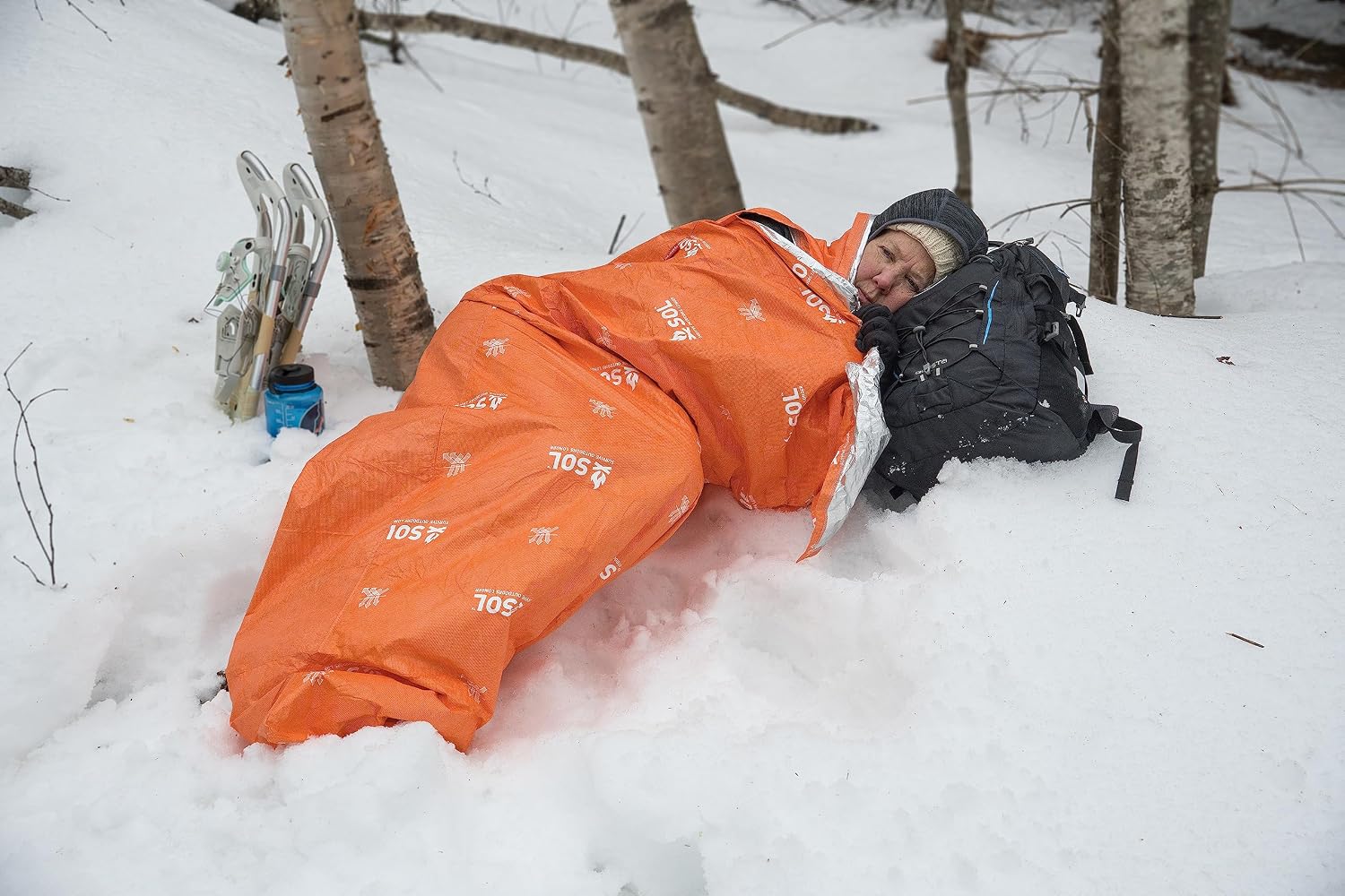 Randonneuse allongée dans la neige dans le sac de bivouac SOL Escape Lite, la tête sur son sac à dos