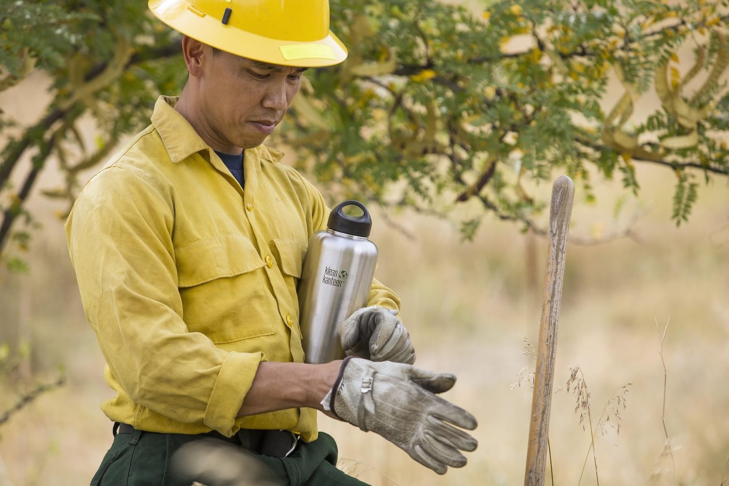 Homme en chemise de travail enfilant ses gants, gourde Klean Kanteen Wide à bouchon Loop Cap sous le bras