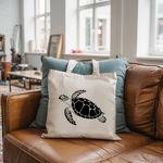 Tote bag femme avec illustration d’une tortue marine nageant en flocage monochrome noir posé sur un canapé - MARJANE et Cie