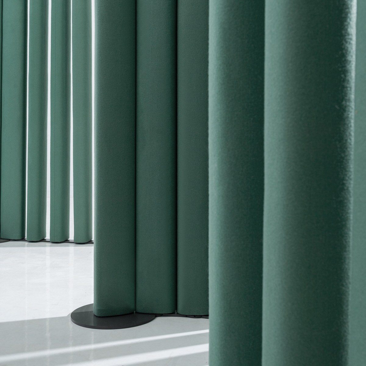 Détail des segments rembourrés en tissu vert et du socle rond noir de la cloison