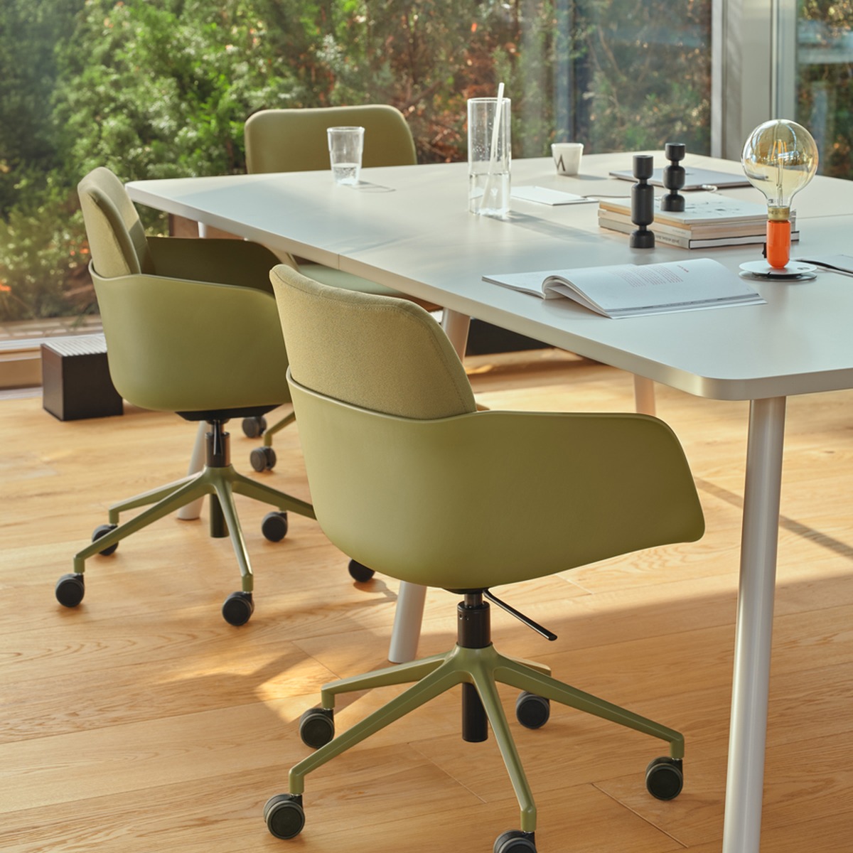Angle dune grande table de réunion beige et pied incliné, avec fauteuils pivotants verts à roulettes