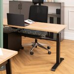 Bureau assis-debout électrique à structure noire et plateau chêne clair dans un bureau