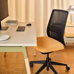 Chaise de bureau résille à assise sépia devant un bureau blanc, près d'un rideau