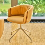 Chaise pivotante tapissée ocre à dossier drapé et placage chêne, vue de trois quarts sur parquet