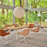 Table de réunion ovale en chêne naturel à pieds blancs dans une salle vitrée ouverte sur un jardin