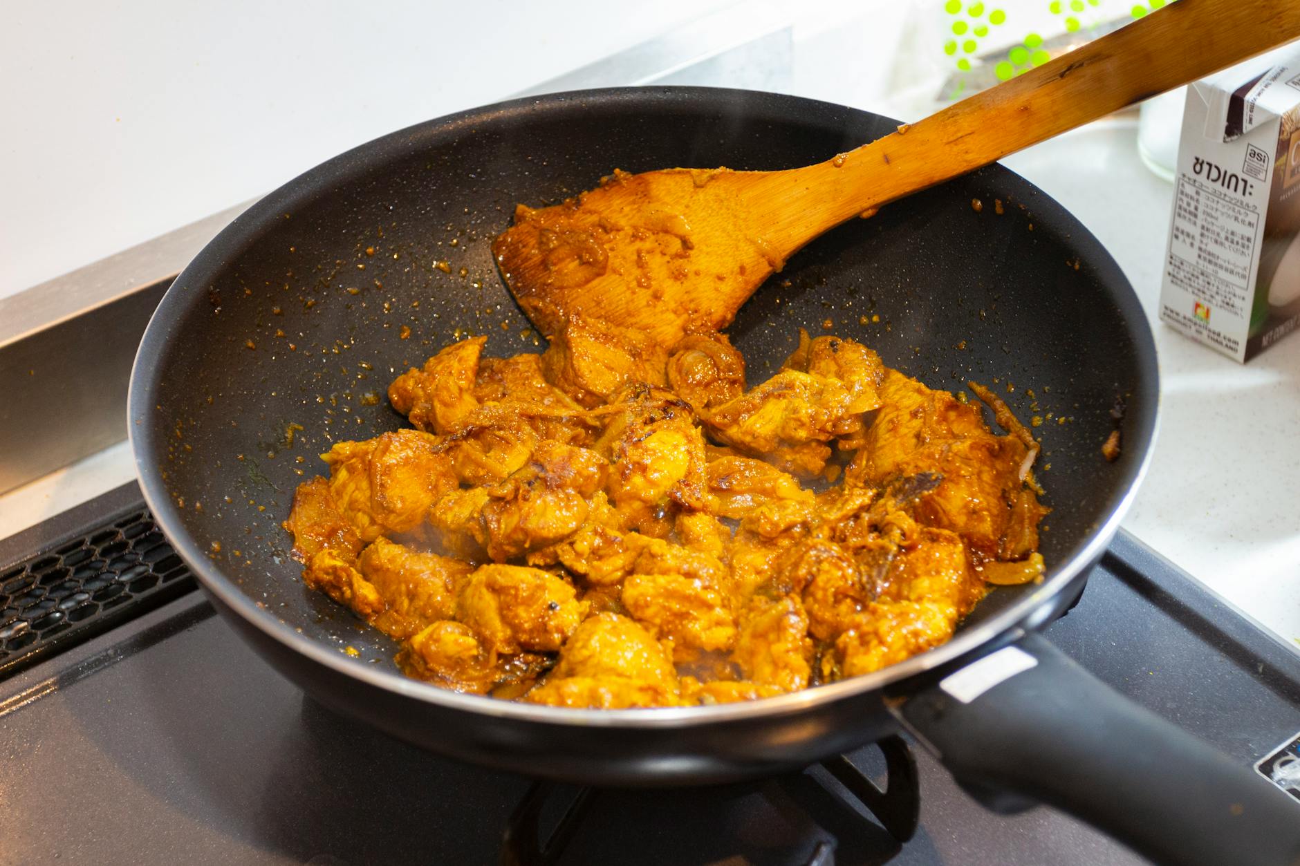 Une poêle remplie de poulet au curry épicé en train de cuire sur une cuisinière, présentant une riche teinte dorée